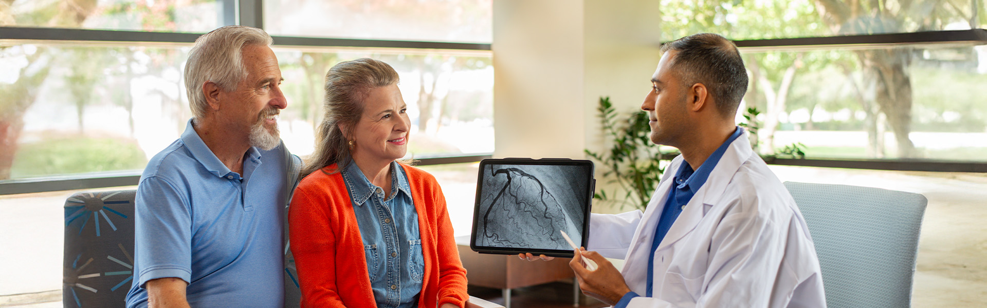 couple talking to physician in waiting room, showing images on tablet