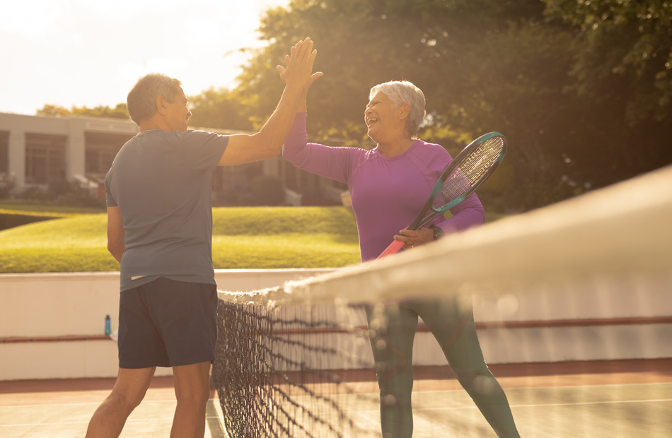 Two adults playing tennis and giving each other a high five on court
