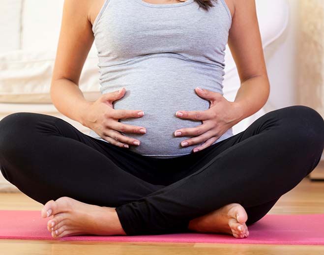 pregnant woman holding belly on yoga mat