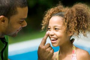 Father applying sunscreen to daughter's nose